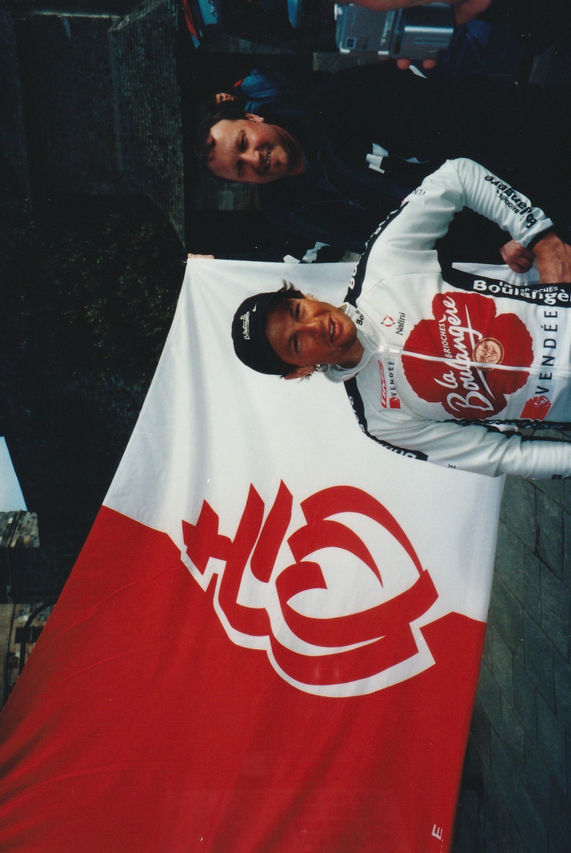 Walter Bénéteau devant un grand drapeau au cœur vendéen, en tenue Brioches La Boulangère